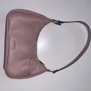 Rosa axelväska från Don Donna i skinn - Snygg axelväska i ljusrosa skinn från Don Donna. Väskan har en stilren, avlång form. Väskan har två mindre fack på utsidan och två större fack på insidan, ett av dessa fack med dragkedja! Perfekt storlek för det viktigaste och enkel att bära över axeln. Enkelt och trendigt val för alla tillfällen.