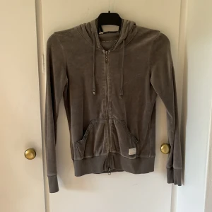 Grå hoodie från Odd Molly med brodyr - Mysig grå hoodie från Odd Molly med dragkedja, huva med snörning och broderad patch på ärmen. Tröjan har ribbade muddar, fickor framtill och mjukt material som känns skönt mot huden. Perfekt för chill dagar eller när du vill ha en avslappnad look.