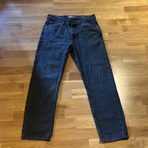 Svarta relaxed fit jeans från Dressmann - Svarta jeans från Dressmann i relaxed fit med raka ben och klassisk femficksdesign. Jeansen har knapp och dragkedja i gylfen. Materialet är robust denim som ger en avslappnad och stilren look.