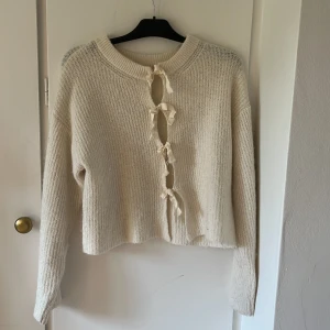 Beige stickad tröja med knyt från Gina Tricot - Superfin beige stickad tröja från Gina Tricot med lång ärm och snygga knytband framtill. Tröjan har en lite croppad passform och är perfekt för lager-på-lager. Mjuk och mysig, passar till både jeans och kjol.