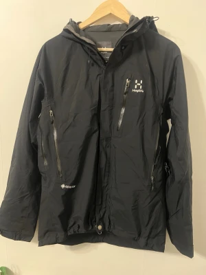 Svart vindjacka från Haglöfs Gore-Tex - Säljer en svart vindjacka från Haglöfs med Gore-Tex-material. Jackan har huva, flera dragkedjeförsedda fickor och justerbar nederkant. Perfekt för dig som vill ha en funktionell och stilren jacka till vardags eller äventyr.