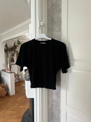 Svart croppad t-shirt från 157 - En svart t-shirt från 157 i storlek XS. T-shirten har korta ärmar och en tight passform vid midjan med enkel, clean design. Perfekt till jeans eller kjol för en chill look. Tillverkad i mjuk bomull som känns skön mot huden.