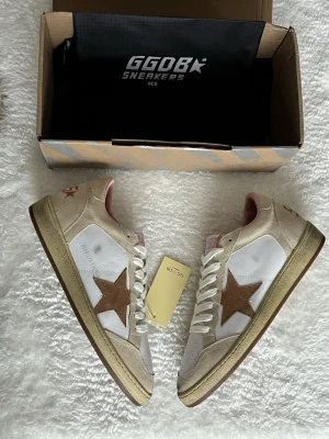 GGDB sneakers med beige och bruna detaljer - Säljer ett par GGDB sneakers i vitt skinn med beige mockadetaljer och brun stjärna på sidan. Skorna har rosa innerfoder och GGDB-logga på plösen. Sulan är beige med vintage-look och snörningen är vit. Perfekta för dig som gillar streetstyle och unika detaljer.