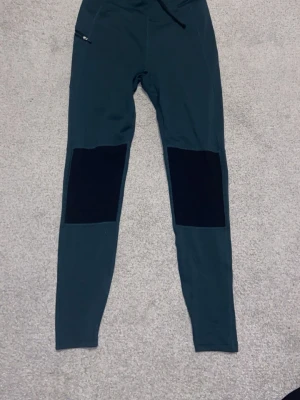 Mörkgröna tights från McKinley XS - Tights från McKinley i mörkgrönt med svarta förstärkningar på knän och bak. De har en liten dragkedjeficka på sidan och är tillverkade i stretchigt syntetmaterial. Perfekta för utomhusaktiviteter eller träning. Varit använda 2-4 gånger, säljer för att de är för små för mig nu. Meddela om ni har några frågor.✨
