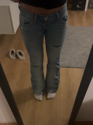 Ljusblå lågmidjade bootcut jeans med slitningar - Säljer ett par ljusblå jeans med bootcut passform och som har slitningar vid knäna och lår och är jätte lång midjade! Jeansen har inga defekter och är använda endast en gång!Skriv gärna om ni har några frågor mvh Alice 