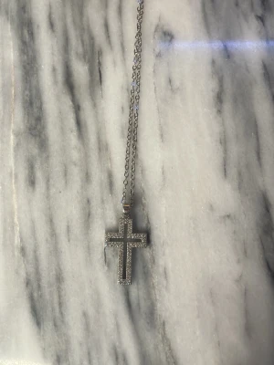 Silverfärgat korshalsband med små kristaller  - Snyggt halsband i silverfärg med ett korsformat hänge täckt av små glittrande kristaller. Kedjan är tunn och justerbar, perfekt för att ge en stilren och trendig touch till din outfit.