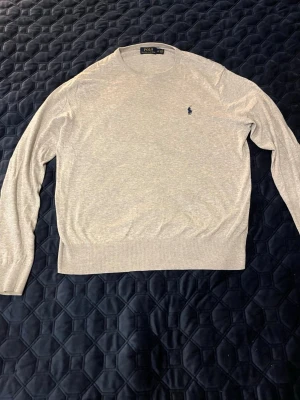 Ljusgrå tröja från Polo Ralph Lauren - Säljer en stilren ljusgrå tröja från Polo Ralph Lauren med rund halsringning och diskret broderad logga på bröstet. Tillverkad i mjuk bomull och kashmirblandning, perfekt för dig som gillar klassisk och clean stil. Långärmad modell med ribbade muddar. Tar gärna byten