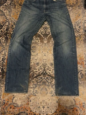 Blå raka jeans från BOSS - Säljer ett par klassiska blå jeans från BOSS med raka ben och normal passform. Jeansen har fem fickor. Materialet är slitstarkt jeans och färgen är en tvättad blå ton. Perfekta för dig som gillar en enkel och tidlös look. Smått slitna i skrevet men går att sy lätt.