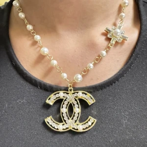 Chanel halsband med pärlor och CC-hänge - Lyxigt halsband från Chanel med stora vita pärlor, guldfärgad kedja och ikoniskt CC-hänge dekorerat med pärlor och stenar. Halsbandet har även ett korsformat smycke med kristaller och pärla. Perfekt statement piece för dig som vill sticka ut.Kvitto finns inte jag själv har köpt den second hand 