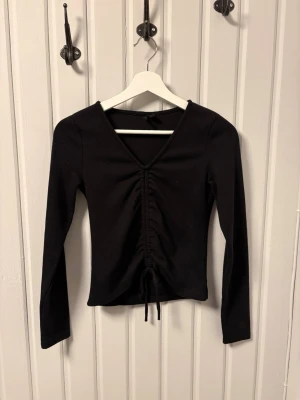 Svart ribbad topp från Vero Moda - En svart långärmad topp från Vero Moda i storlek XS. Toppen har ribbad struktur, v-ringning och snörning framtill som ger en snygg detalj🤩 Materialet är mjukt och stretchigt, perfekt till många olika outfits😊Går jättebra att använda "Köp nu"! Vi skickar inom 1-2 dagar💕 Bara att skriva vid funderingar🤗