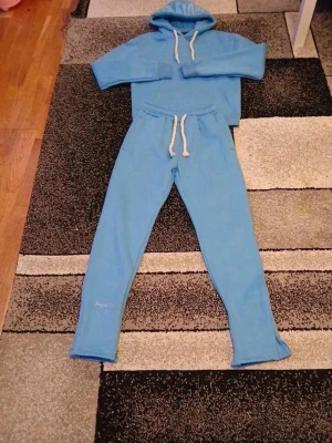Ljusblått mjukisset – hoodie & mjukisbyxor - Ljusblått mjukisset i mycket fint skick. Setet består av en hoodie med huva och vita dragsnören samt matchande mjukisbyxor med resår och dragsko i midjan. Mjukt och bekvämt material som passar perfekt för vardag, skola eller hemmabruk. Stilren design och skön passform. Använd fåtal gånge
