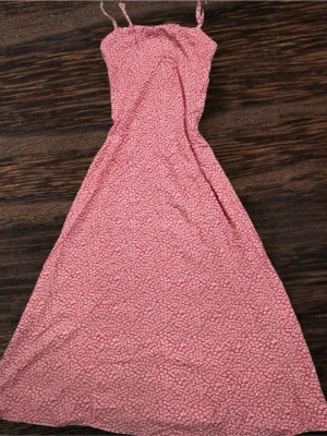 Rosa blommig långklänning Divided - Vi kan diskutera priset. Supersöt långklänning från Divided i rosa med små vita blommor. Klänningen har smala axelband och en lätt utställd passform som ger en flowy känsla. Perfekt för varma dagar och somriga vibes!