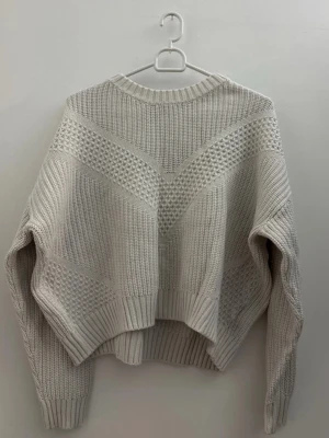 Vit stickad tröja med strukturmönster - Säljer en vit stickad tröja med snygga strukturmönster och ribbade muddar. Tröjan har en relaxed fit och lång ärm, perfekt för lager på lager under kyliga dagar. Passar dig som gillar en enkel men ändå detaljerad look.