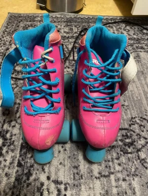 Roces rosa rullskridskor EU 37 - Säljer ett par färgglada rullskridskor från Roces i storlek 37. Skorna är rosa med blå detaljer, blå snörning och blå hjul. Insidan är fodrad i blått tyg och det finns vita och rosa detaljer samt ett snöflingemönster på sidan. Perfekta för dig som vill sticka ut på rinken!