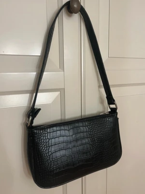 Svart axelväska  - Säljer en svart axelväska i croco-imitation