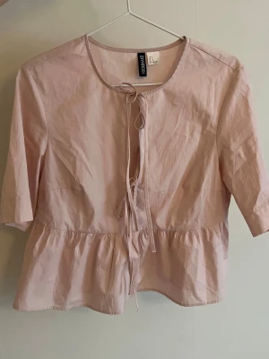 Ljusrosa blus med rosetter  - Supersöt ljusrosa blus med knyt framtill och volang nedtill. 