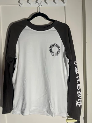 Chrome Hearts långärmad t-shirt - Säljer en långärmad t-shirt från Chrome Hearts med svartvita kontraster. Tröjan har svart tryck på bröstet, ryggen och längs ärmarna. Klassisk baseballmodell med svarta ärmar och vit kropp. Tillverkad i mjuk bomull och har en avslappnad passform.