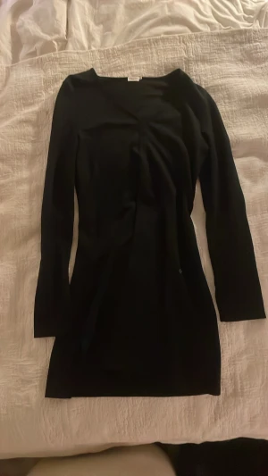 Svart långärmad klänning Filippa K - En lite kortare stilren svart kortklänning från Filippa K i storlek M. Klänningen har lång ärm och v-ringning, vilket ger en enkel men elegant look. Materialet känns mjukt och följsamt, perfekt för dig som gillar minimalistisk design.