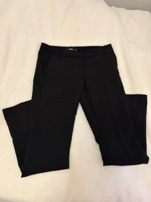 Svarta kostymbyxor från BikBok - Säljer ett par klassiska svarta kostymbyxor från BikBok i storlek 38. Byxorna har raka ben, bälteshällor och diskreta fickor. Perfekta till en stilren och clean look. Materialet känns mjukt och följsamt. (Allting tvättas innan leveran)
