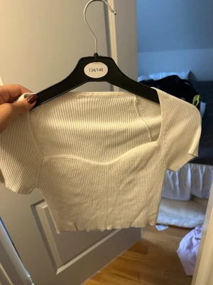 Vit ribbad croppad topp - Säljer en vit ribbad croppad topp med korta ärmar och fyrkantig urringning. Toppen är i stretchigt material och har en figurnära passform som framhäver siluetten. Perfekt till jeans eller kjol för en trendig look.