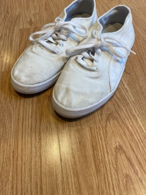 Vita sneakers från Puma strl 37 - Säljer ett par klassiska vita sneakers från Puma i storlek 37. Skorna har snörning, rund tå och ovandel i canvas med vit sula. Perfekta till jeans eller shorts för en clean och sportig look. Puma-logga på plösen och sidan.