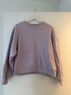 Ljuslila sweatshirt från Gina Tricot - En ljuslila sweatshirt från Gina Tricot med rund halsringning och ribbade muddar vid ärmslut och nederkant. Perfekt för chill dagar och enkel att styla med jeans eller leggings.