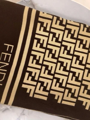 Beige och brun stickad väst från Fendi - Säljer en snygg stickad väst från Fendi i beige och brunt med det klassiska FF-mönstret över hela plagget. Västen har tydliga ränder och logotypen Fendi invävd på framsidan. Perfekt för dig som vill ha en statement piece i garderoben.