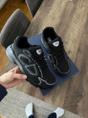 Svarta Dior B30 sneakers - Säljer ett par svarta Dior B30 sneakers med reflekterande detaljer och tydlig Dior-logga på sidan och hälen. Skorna har snörning, meshpaneler och en chunky sula för extra street vibe. Perfekta för dig som vill ha en exklusiv och modern look.