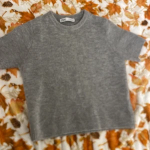 Grå stickad tröja från Zara - Säljer en enkel och stilren grå stickad tröja från Zara i storlek S. Tröjan har korta ärmar och rund halsringning med ribbade detaljer vid hals och ärmslut. Perfekt för dig som gillar en clean look och mjuka material.