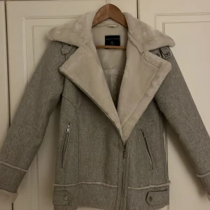 Grå coat från Dorothy Perkins - Säljer en snygg grå teddyjacka från Dorothy Perkins i storlek 34. Jackan har en stor krage i ljus teddy (kragen är vit och ren men i denna belysning ser den bara gråskiftabde ut :) )dragkedja framtill och två sidofickor med dragkedja. Serena Vanderwoodsen stil! Detaljer med spänne vid axeln och nederkant ger en cool look. Perfekt för kalla dagar!