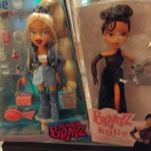 Svart långklänning från Bratz Kylie - Säljer en ikonisk svart långklänning från Bratz Kylie-dockan. Klänningen har en axelbandslös design med transparenta meshärmar och en hög slits på ena sidan. Perfekt för dig som älskar statement-plagg och coola detaljer.