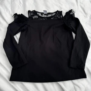 Långärmad topp med spets  - Svart långärmad topp från Lindex med offshoulder-detaljer & spets upptill. Storlek: 134/140. Fraktar inom 24h!
