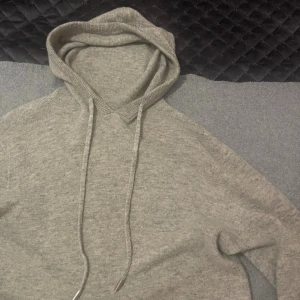 Ljusgrå stickad hoodie med huva - Mysig ljusgrå stickad hoodie med huva och dragsnören med metalländar. Tröjan har lång ärm och ribbade muddar vid ärmslut och nederkant. Perfekt för chill dagar och enkel att matcha med jeans eller mjukisbyxor. Tröjan är ny och få antal gånger använd. Nypris från 600-800kr. Bara skriva vid en fråga mvh Liam!