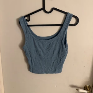 Blå ribbad croppad linnetopp - Säljer en ljusblå croppad linnetopp med breda axelband och ribbad struktur. Toppen är ärmlös och har en enkel, stilren design som är perfekt för varma dagar. Materialet känns mjukt och stretchigt mot huden.