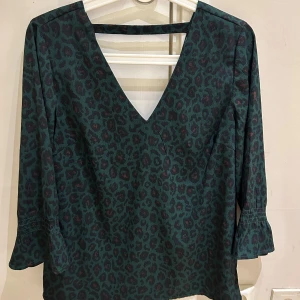 Grön leopardmönstrad blus från VILA - Säljer en grön blus från VILA med leopardmönster i mörka toner. Blusen har v-ringning, trekvartsärmar med lätt volang och smockdetalj vid ärmslut. Materialet är mjukt och lätt, perfekt för dig som gillar att sticka ut med coola mönster.