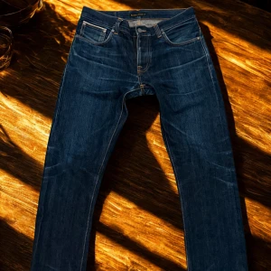 Nudie Jeans – Dry Selvedge W33 L32 - Nudie Jeans Grim Trim – Dry Selvedge Storlek W33 L32. 100 % japansk/italiensk bomull 🇯🇵🇮🇹 Rå denim av högsta kvalitet – formar sig perfekt efter dig med tiden ✨ I mycket bra skick, knappt använda ✅ Nypris ca 2500 kr. Pris kan diskuteras vid snabb affär 💬 Hör av dig för fler bilder ✉️ Midja: Ca 42 cm, Gylf till ankel: Ca 73 cm, Helhetslängd: Ca 100 cm, Lårbredd: Ca 27 cm