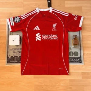 Liverpool röd fotbollströja Adidas - Röd Liverpool fotbollströja från Adidas med vita detaljer och klubbmärke på bröstet. Tröjan har korta ärmar, tryckt sponsorlogga och Champions League-märke på ärmen. Tillverkad i lätt funktionsmaterial för bästa komfort.
