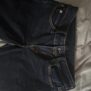 Bootcut jeans från Cheap Monday - Mörkblå bootcut jeans från Cheap Monday med kontrasterande gula sömmar och klassiska fem fickor. Jeansen har en snygg passform och är tillverkade i denim med en cool etikett med rosa text bak. Perfekta för dig som gillar en retro vibe.