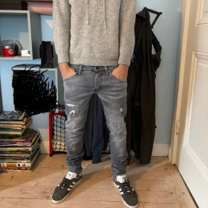 Grå slitna jeans med skinny fit - Säljer ett par grå jeans med slitningar och trasiga detaljer på benen från Jack and Jones. Jeansen har en slim passform och klassisk femficksdesign. Snyggt tvättade med en lite ljusare grå ton och dragkedjegylf. Perfekta för en avslappnad streetstil.