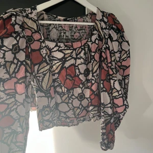 Blommig blus från Gina Tricot - Säljer en blommig blus från Gina Tricot med puffiga långärmar och smockad rygg. Färgerna går i rosa, rött, beige och svart med ett stort blommönster. 