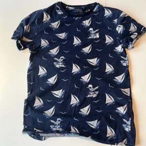  t-shirt  från Polo Ralph Lauren - Mörkblå t-shirt från Polo Ralph Lauren med custom slim fit. T-shirten har ett marint mönster med vita segelbåtar och fåglar samt broderad logga på bröstet. Perfekt för dig som gillar en avslappnad men ändå stilren look. Står S men funkar nog också på XS. Pris går att diskuteras såklart 👍 