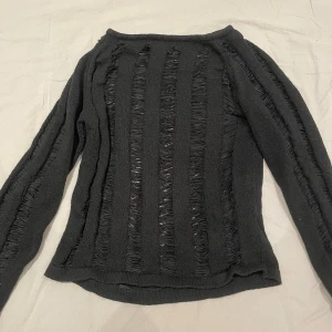 Svart stickad tröja med slitsade detaljer - Svart stickad tröja med lång ärm och coola slitsade detaljer i vertikala ränder både fram och på ärmarna. Tröjan har en smal passform och är perfekt för dig som gillar en edgy stil. 