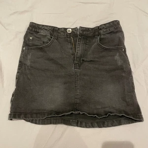 Svart jeanskjol med fickor - Snygg svart jeanskjol med klassisk femficksdesign och dragkedja framtill. Kjolen har bälteshällor. Perfekt att matcha med en t-shirt eller hoodie för en trendig stil.