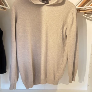 Beige hoodie i kashmir från Oscar Jacobson - Säljer en supermjuk beige hoodie från Oscar Jacobson i lyxig kashmir. Tröjan har huva, ribbade muddar och lång ärm. Perfekt för dig som vill ha en stilren och bekväm look med premiumkänsla.