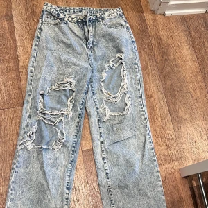 Ljusblå ripped jeans med loose fit - Säljer ett par ljusblå jeans med rejält slitna hål på båda benen framtill. Jeansen har en loose passform och raka ben, klassisk femficksmodell och stentvättad look. Perfekta för dig som gillar en avslappnad och edgy stil.