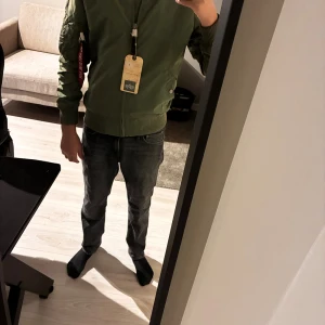 Grön bomberjacka Alpha Industries S - Säljer en grön bomberjacka från Alpha Industries i storlek S. Jackan har klassisk MA-1 design med ribbade muddar, orange foder och ikonisk 'Remove Before Flight'-tag på ärmen. Materialet är slitstark polyester och jackan har dragkedja framtill samt fickor med tryckknappar. Helt ny, har inte använt den något pga för liten . Jackan är liten i storleken vilket gör att XS passar perfekt 