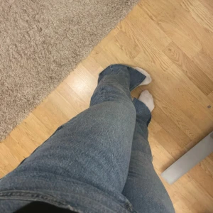 Blå bootcut jeans med slits - Säljer ett par blå jeans med bootcut-modell och snygga slitsar nertill på benen. Jeansen har normal midja och klassisk femficksdesign. Materialet är jeans i bomull och passformen är normal med lite utsvängda ben. Perfekta för dig som gillar en trendig och avslappnad look. Jag är ca 162
