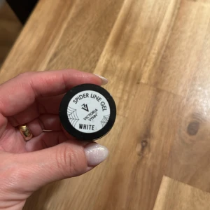 Spider Line Gel White från Victoria Vynn - Spider Line Gel i färgen vit från Victoria Vynn, perfekt för att skapa tunna och kreativa linjer på naglarna. Kommer i en liten rund svart plastburk med vit etikett och spindelnätsdesign. Gelen är enkel att använda för nail art och detaljerade mönster.