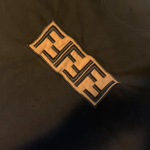 Svart Fendi t-shirt med logga - Svart t-shirt från Fendi i 100% bomull med klassisk rund hals och korta ärmar. På bröstet sitter en broderad beige Fendi-logga med svarta detaljer, vilket ger en lyxig och stilren vibe. Perfekt för dig som gillar designer och vill sticka ut.