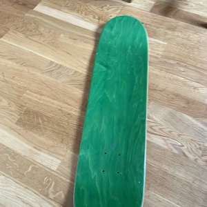 Brädkultur Beach Club Stockholm 1628 Skateboard Deck - Unik skateboarddeck från Brädkultur Beach Club med färgstark grafik av skepp och skelett, Stockholm 1628. Oanvänd, inga synliga skador eller slitage. Perfekt för samlare eller åkning. Grön ovansida, signerat på undersidan.som inte säljs längre 